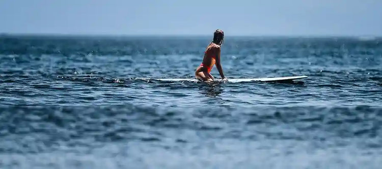 A surfer sitting on her board, waiting on the water at Playa Venao