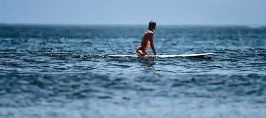 A surfer sitting on her board, waiting on the water at Playa Venao